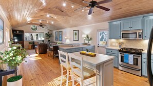 Una cocina amplia con vigas de madera en el techo, una isla central con taburetes de bar, un microondas, estufa y refrigerador.