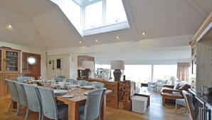 A spacious living area with a high ceiling and skylight, a dining area with a wooden table and chairs, and a cozy seating area with a sofa and armchairs. - Penmorfa - Sublime Abersoch retreat with roof terrace, 80m from beach, great for surfing (Abersoch)