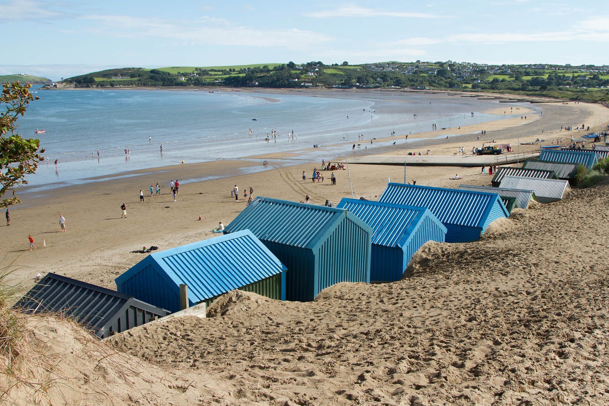 A beach with people and a row of blue beach huts.