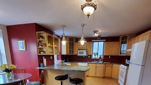 Een keuken met houten kastjes, een centraal eiland met krukken, een koelkast en een magnetron.