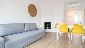 Ett modernt vardagsrum med en grå soffa, gula stolar, ett vitt matbord och en hängande lampa.