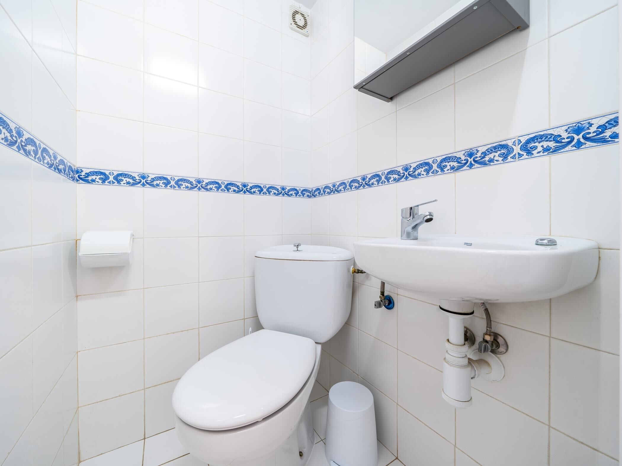 Un baño con azulejos blancos, un inodoro, un lavamanos y un dispensador de toallas de papel.