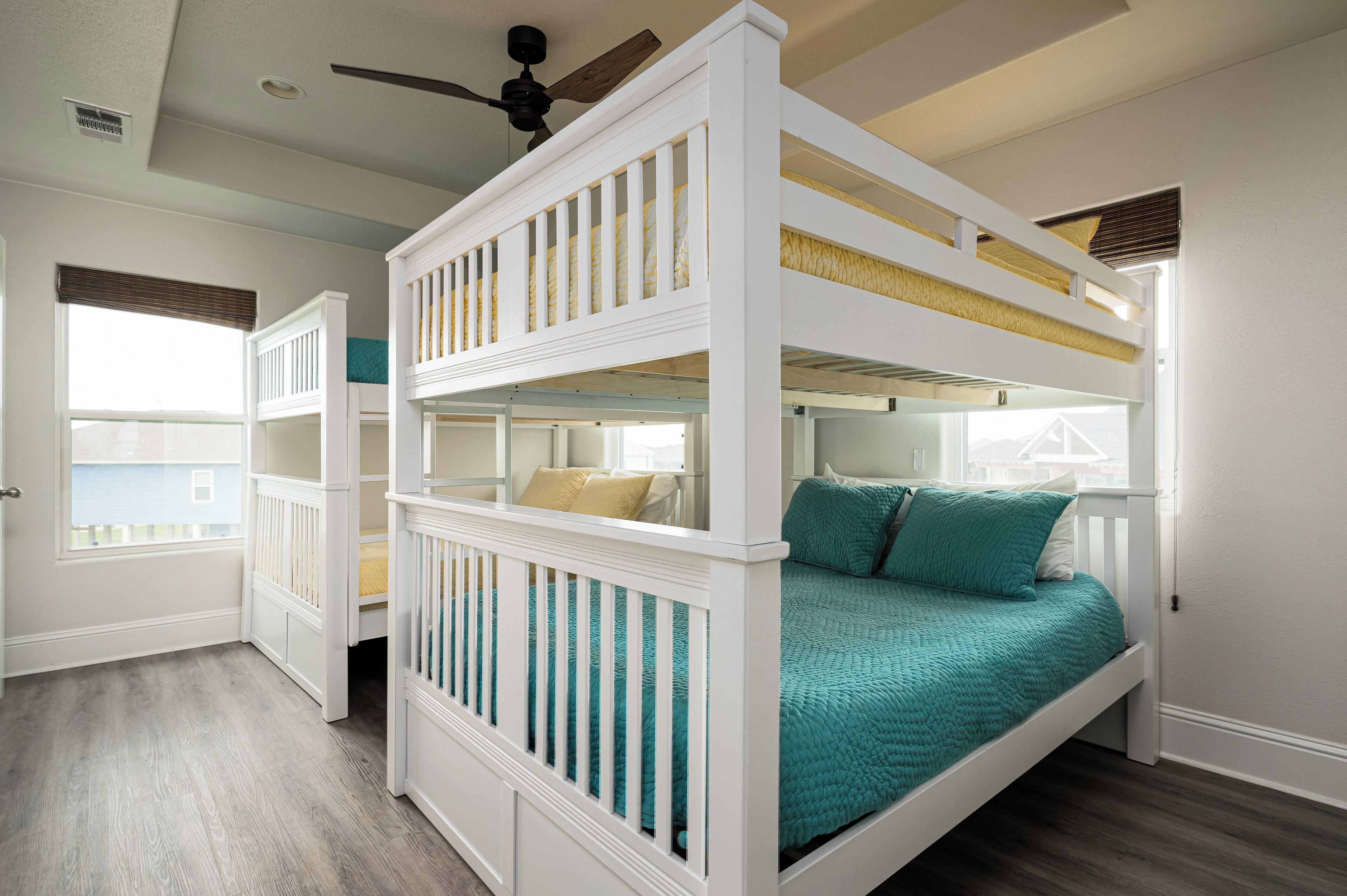 A bunk bed room with a ceiling fan, a window with blinds, and a door.