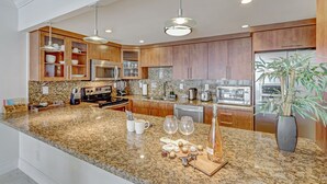 A modern kitchen with granite countertops, wooden cabinets, stainless steel appliances, and pendant lighting. - OCEAN RESERVE LUXURIOUS CONDO 2MIN AWAY FROM BEACH (Sunny Isles Beach)