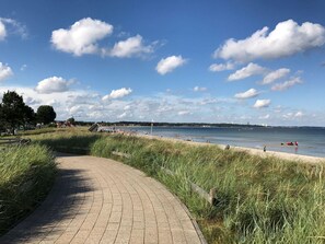 Un vialetto lastricato che conduce a una spiaggia, con cielo sereno e nuvole.