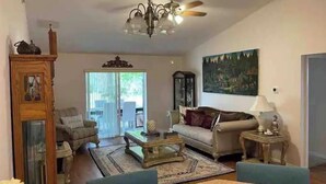 Uma sala de estar espaçosa com um lustre, um ventilador de teto, uma grande pintura e um espaço de jantar com mesa e cadeiras.