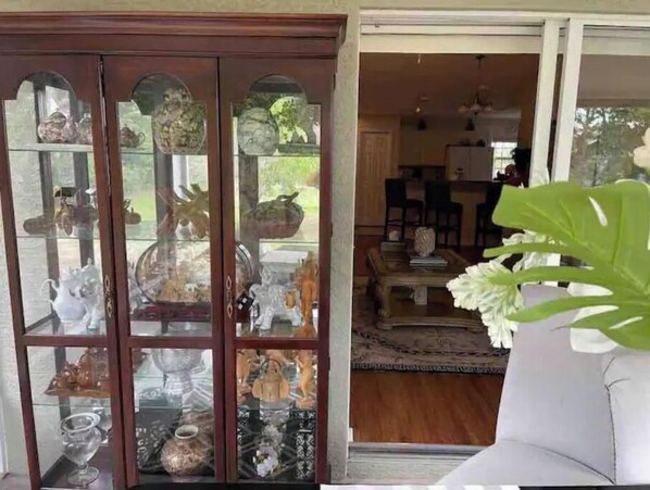 A room with a glass display cabinet filled with decorative items, a white sofa, and a large plant.