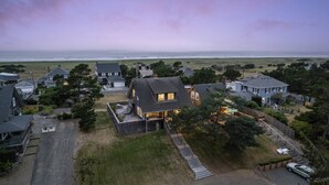 An aerial view of a coastal residential area with houses, a grassy field, and the ocean in the background.