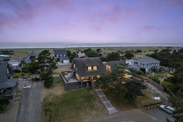 An aerial view of a coastal residential area with houses, a grassy field, and the ocean in the background.