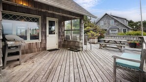 A wooden deck with a grill, a covered seating area, and a stone building in the background.