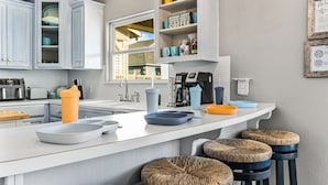 A modern kitchen with white cabinets, a central island with stools, and a window providing natural light. - Family Fun! ⛱ Walk to Beach ♥Pet-Friendly (Crystal Beach)