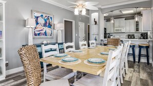 A modern kitchen with white cabinets, a wooden dining table set with blue plates, and a ceiling fan. - Family Fun! ⛱ Walk to Beach ♥Pet-Friendly (Crystal Beach)