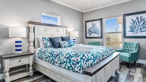 A bedroom with a bed, nightstands, a chair, and artwork on the walls. - Family Fun! ⛱ Walk to Beach ♥Pet-Friendly (Crystal Beach)