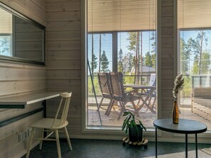 A room with a wooden interior, a window with blinds, a chair, a small table with a vase, and a plant.