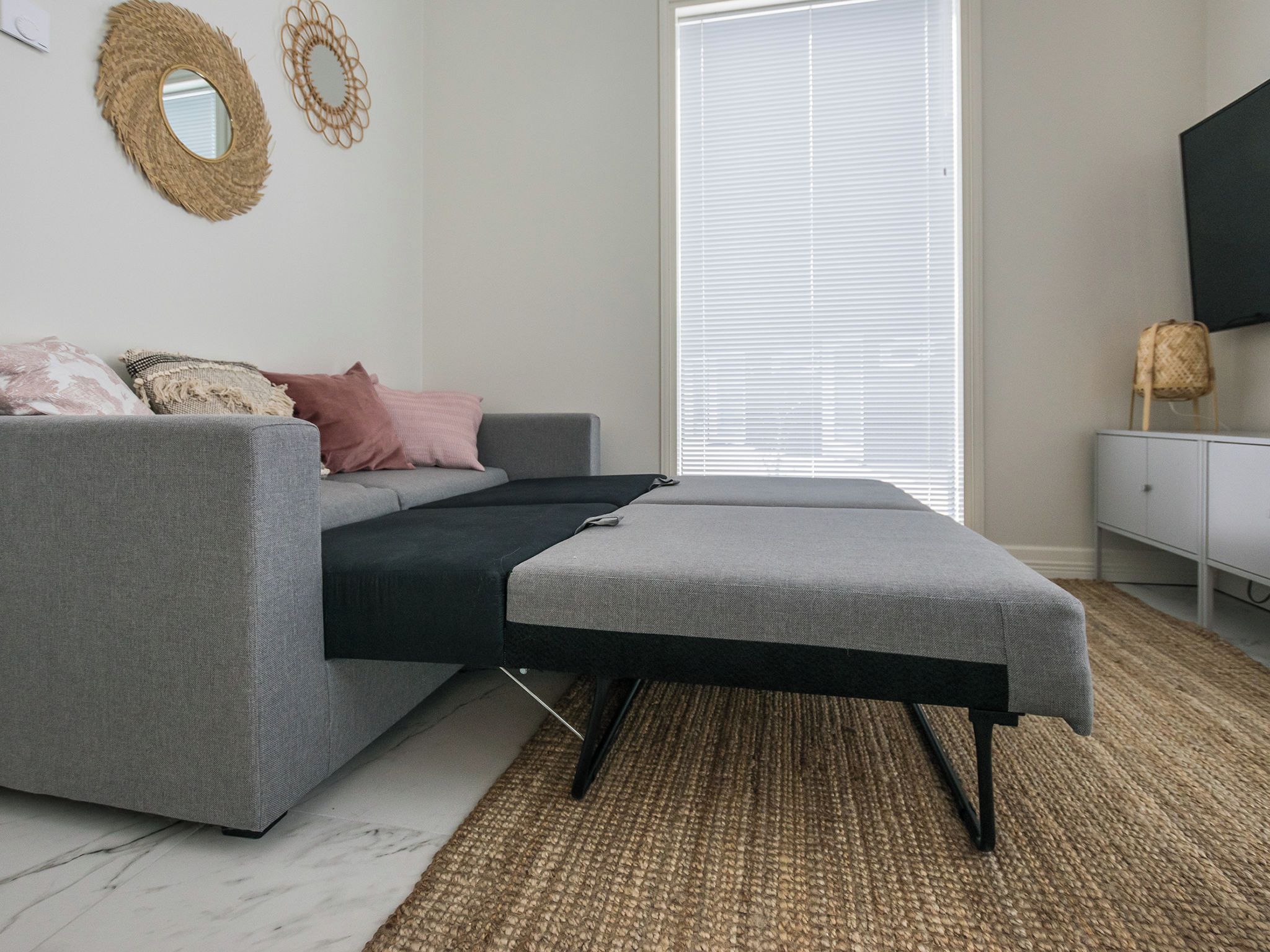 Ein modernes Wohnzimmer mit einem grauen Sofa, einem schwarzen Hocker und einem Webteppich.