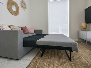Ein modernes Wohnzimmer mit einem grauen Sofa, einem schwarzen Hocker und einem Webteppich.