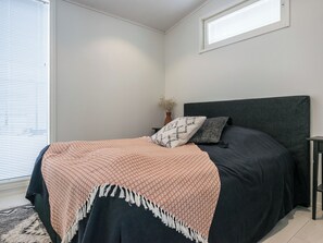 A bedroom with a bed, a nightstand, a window with blinds, and a small vase with dried flowers. - Villa kuortane by Interhome (Kuortane)