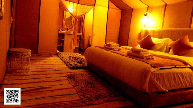 A tented room with a bed, pillows, a nightstand, a mirror, and a small stool.