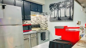 Una cocina con refrigerador, microondas, tostadora y pileta roja.