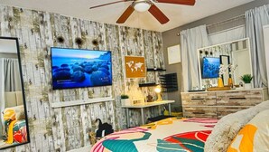 Un dormitorio con una cama grande, ventilador de techo, televisor montado en la pared y un cuadro con un mapa del mundo.