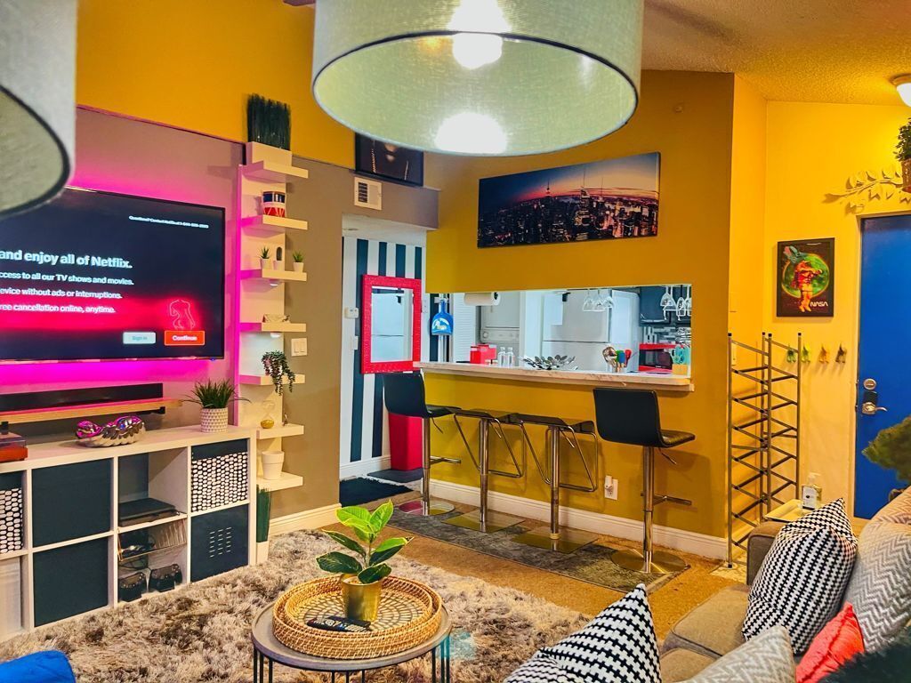 A modern living room with a flat-screen TV, a kitchen area, and a dining space.