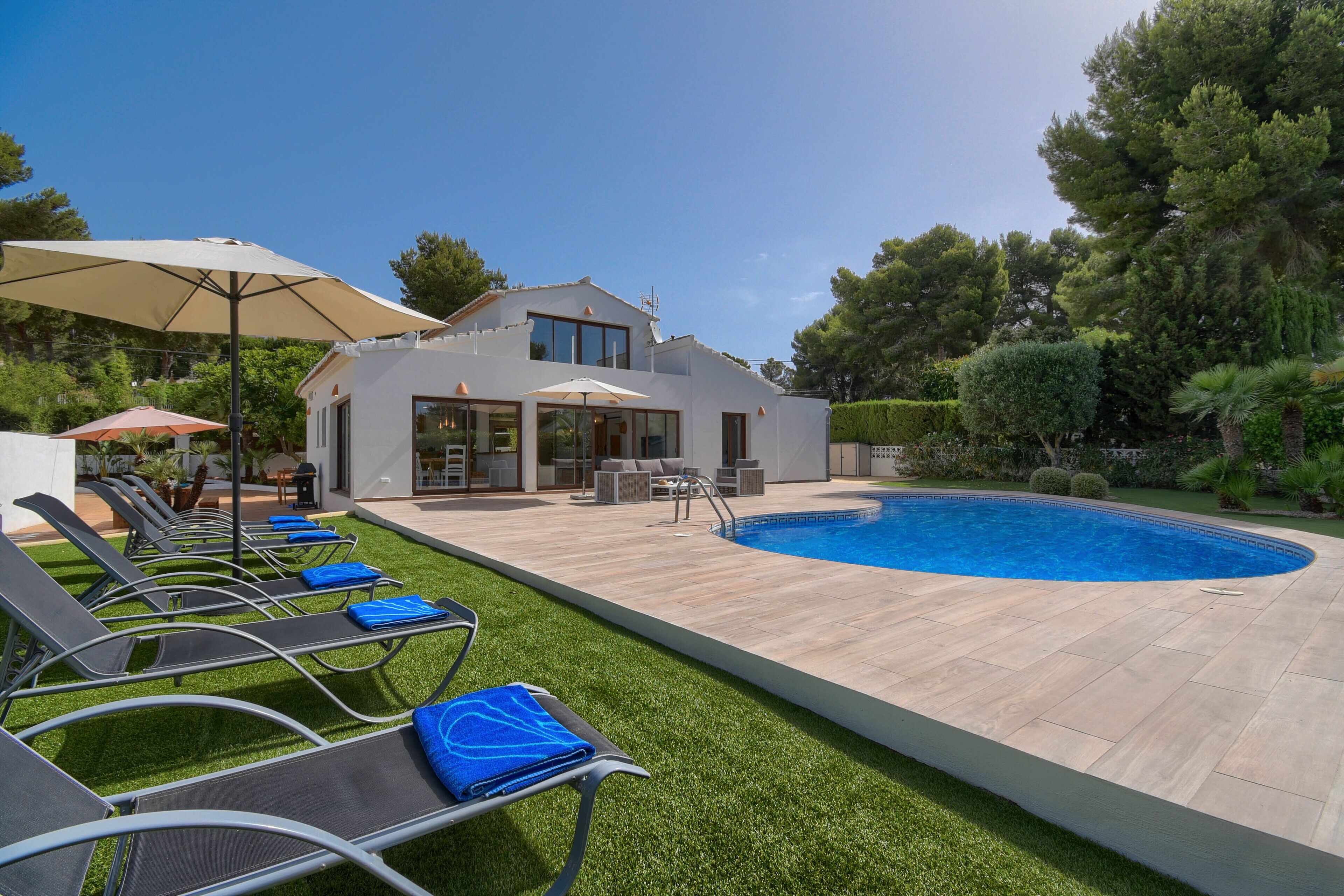 A modern house with a swimming pool, outdoor seating, and a well-maintained lawn.