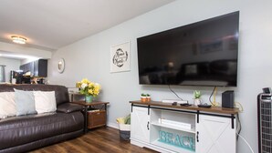 A living room with a brown leather sofa, a white entertainment unit with a flat-screen TV, and a wooden coffee table. - Next to Kayak Park |1st Floor Condo |Short Walk to Beach |Beach Cart, 2 Chairs & Umbrella |Dogs Ok (Fort Walton Beach)