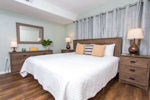 Een slaapkamer met een groot bed, twee nachtkastjes met lampen, een dressoir, een spiegel en een kamerplant.