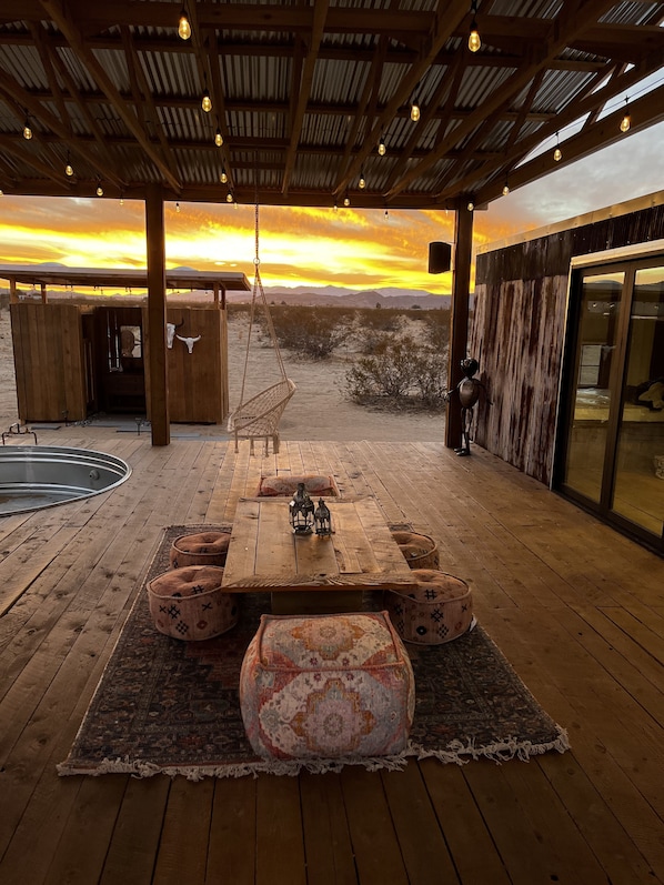 Une terrasse en bois avec une table et des chaises, une balançoire suspendue et une vue sur le désert au coucher du soleil.