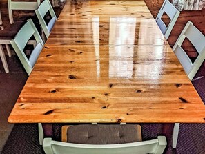 Une longue table en bois, entourée de chaises des deux côtés, se trouve dans une pièce dont le sol est recouvert d’un tapis à motifs.