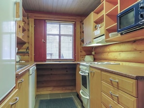 Una cocina compacta con armarios de madera, microondas y ventana con persianas.