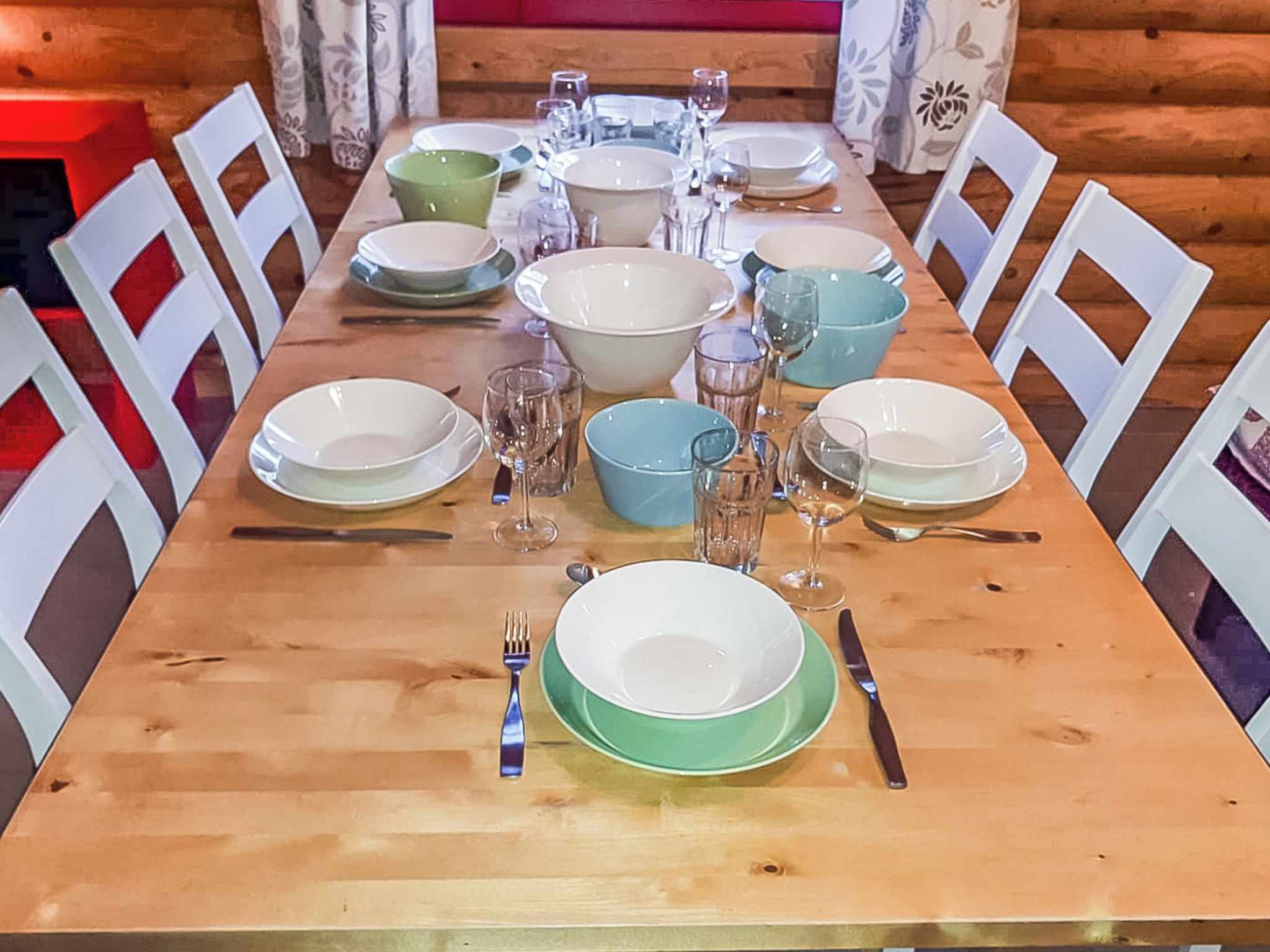 A wooden dining table set with plates, bowls, glasses, and cutlery.