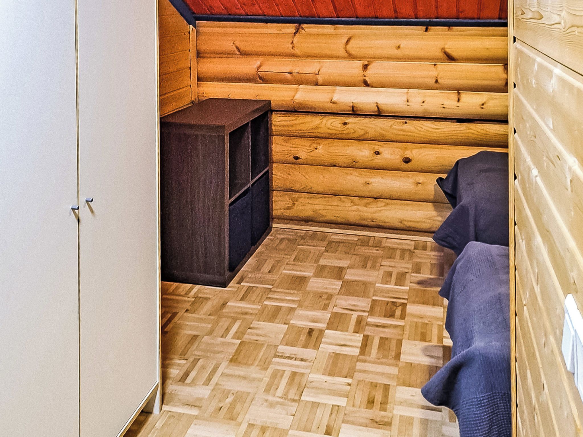 A log cabin interior with a wooden floor, a small dark wooden cabinet, and a blue towel on a bench.