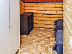 L’intérieur d’une cabane en rondins, avec un plancher en bois, une petite armoire sombre en bois et une serviette bleue posée sur un banc.