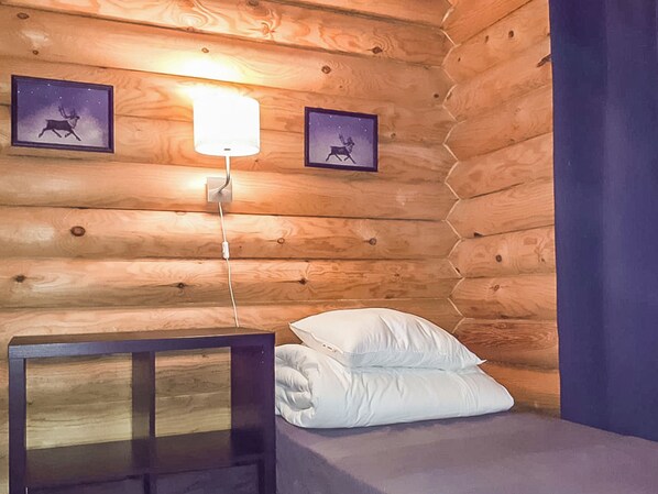 A wooden cabin room with a bed, pillows, a nightstand, and two framed pictures on the wall.
