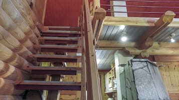 A wooden staircase with a handrail, leading to a room with a stone fireplace.