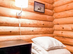 Habitació d'una cabana de fusta amb un llit, una làmpada penjada a la paret i un quadre amb marc.