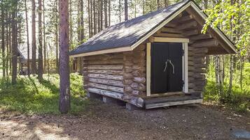 A small log cabin with a sloped roof and a single door, surrounded by a forest.