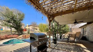 Un patio trasero con una parrilla, una piscina y un área de porche techado.