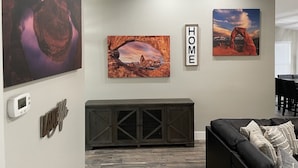 Un salon avec un meuble console en bois foncé, un canapé en cuir noir et trois tableaux représentant des paysages, encadrés et accrochés au mur.