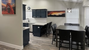 Une cuisine moderne avec des meubles de couleur sombre, un plan de travail blanc et un coin repas comprenant une table et des chaises.