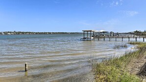 A clear view of a lake with a wooden pier extending into the water, a gazebo on the pier, and a grassy shoreline. - Stylish Gulf Shores Getaway w/ Dock Access! (Gulf Shores)