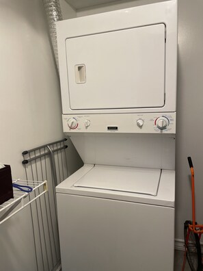 Un appareil compact, blanc, combinant une machine à laver et un sèche-linge à chargement frontal, doté de boutons de commande pour différents programmes de lavage.