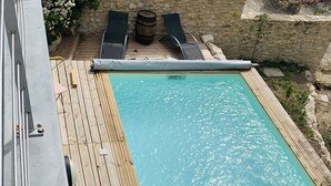 Ein rechteckiger Pool mit Holzterrasse, zwei Liegestühlen und einem kleinen Fass.