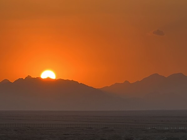 A sunset over a beach with mountains in the background.