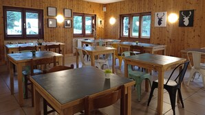 A wooden-paneled room with multiple tables and chairs, large windows, and framed pictures on the walls. - Hotel Fior di Roccia Valmalenco (Lanzada)