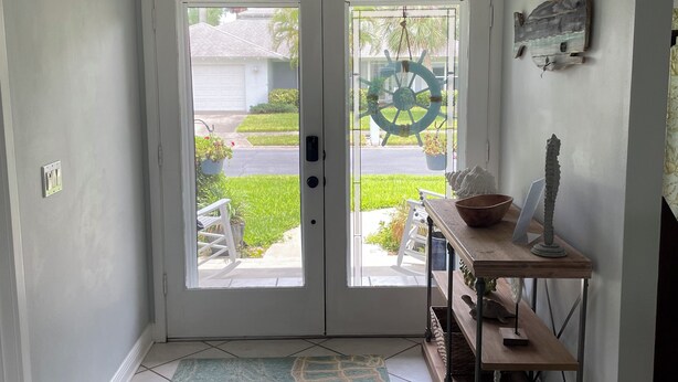 A hallway with a double door leading to a patio, a wooden bench, a wall-mounted ship's wheel, and a small table with a bowl and a candle.
