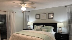 A bedroom with a bed, two nightstands, a ceiling fan, and a window with curtains.