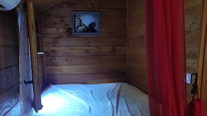 A wooden cabin room with a bed, a framed picture on the wall, and a red curtain. - Caravan (Arles)