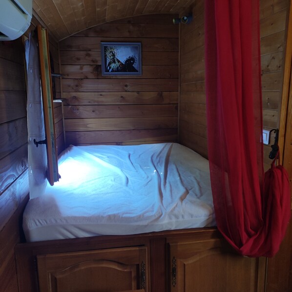 A wooden cabin room with a bed, a framed picture on the wall, and a red curtain.